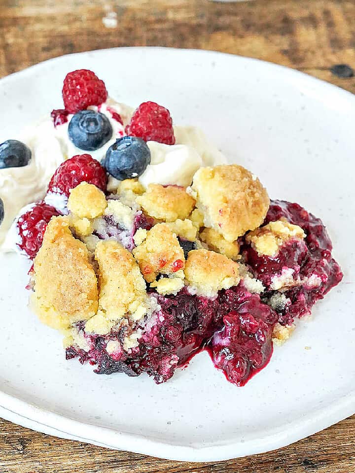 Mixed berry dump cake with cream on a white plate.