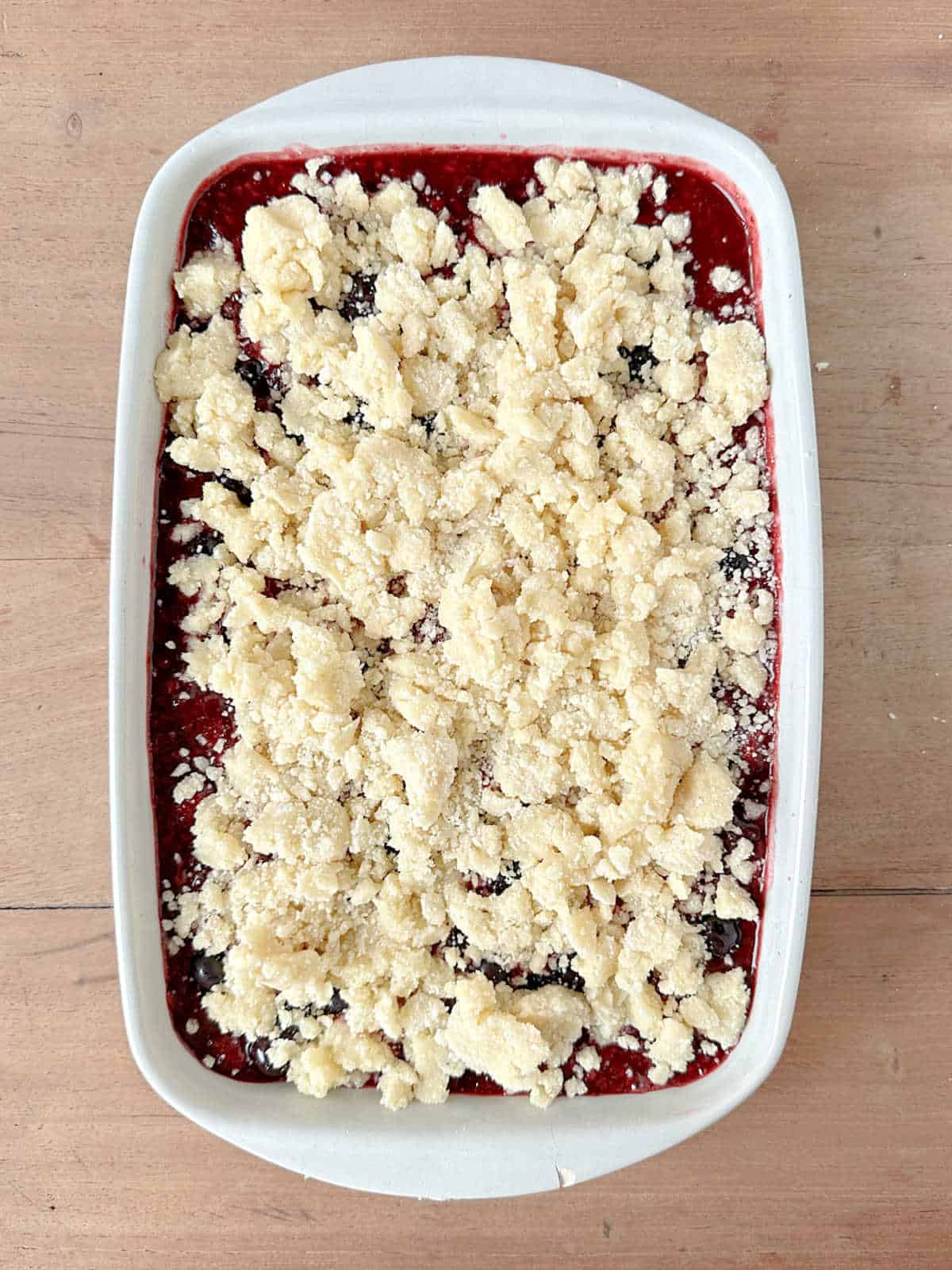 Rectangular baking dish with berry dump cake before baking on a wooden table.