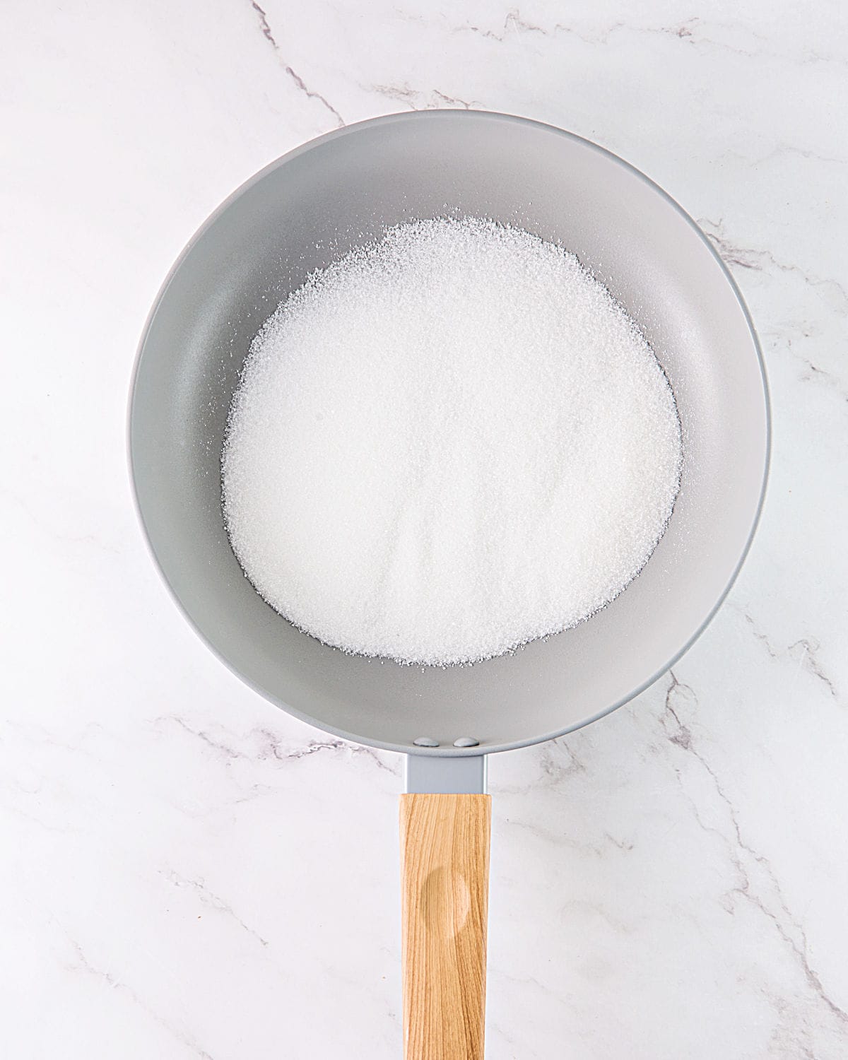 Granulated sugar in a light gray skillet on white marble.