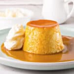Caramel flan with whipped cream on a gray plate. White background.