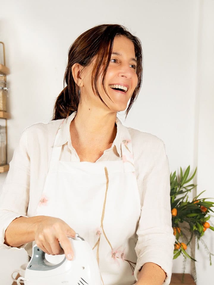 Person with apron laughing in a kitchen with electric mixer in hand.