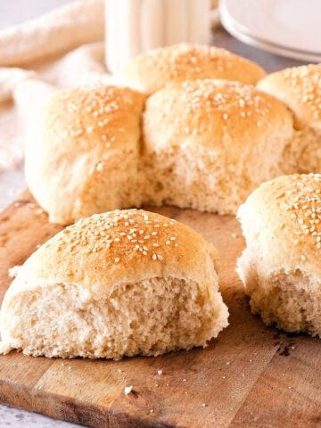 Wooden board with several dinner rolls. White and gray background.