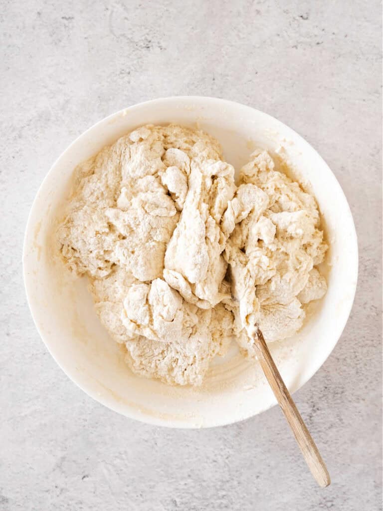 Shaggy mass of bread dough in a white bowl on a gray surface.