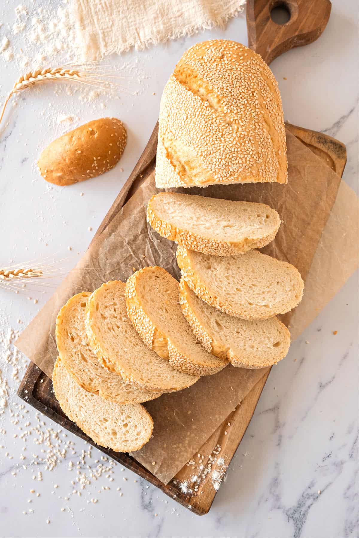 Top view of sliced semolina bread on a wooden board. White marble background.