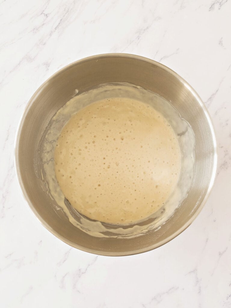 Metal bowl with yeast mixture for bread. White marble background.