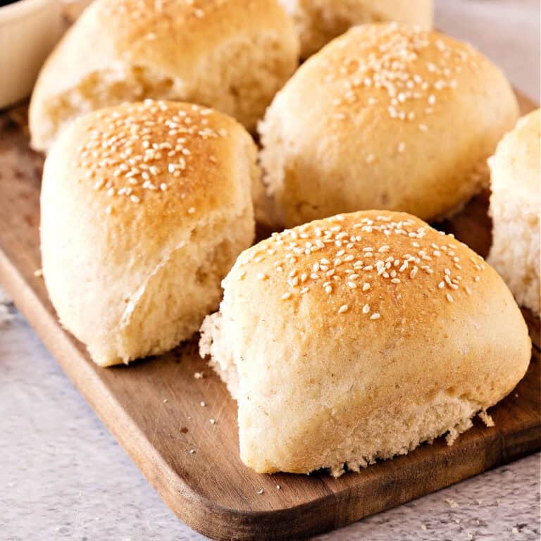 Close up of sesame-topped dinner rolls on a wooden board.
