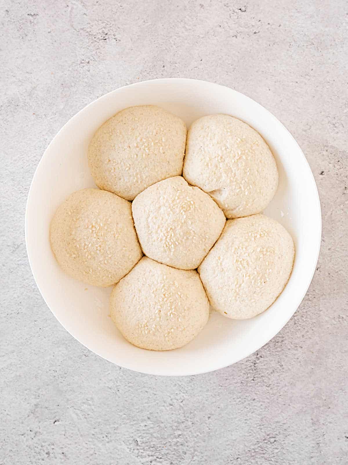 Doubled bread dough balls in a white round dish. Gray surface.