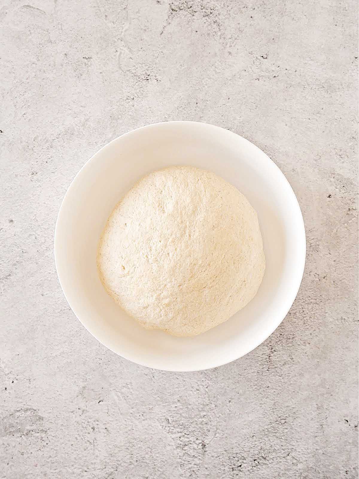 Bread dough ball in a glass bowl on a gray surface.