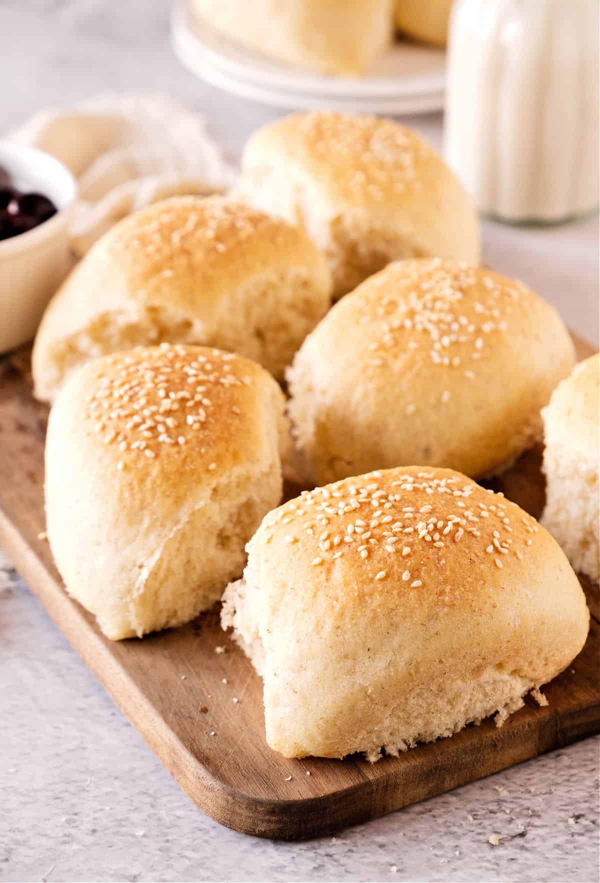 Several sesame-topped bread rolls on a wood board. Light gray surface.