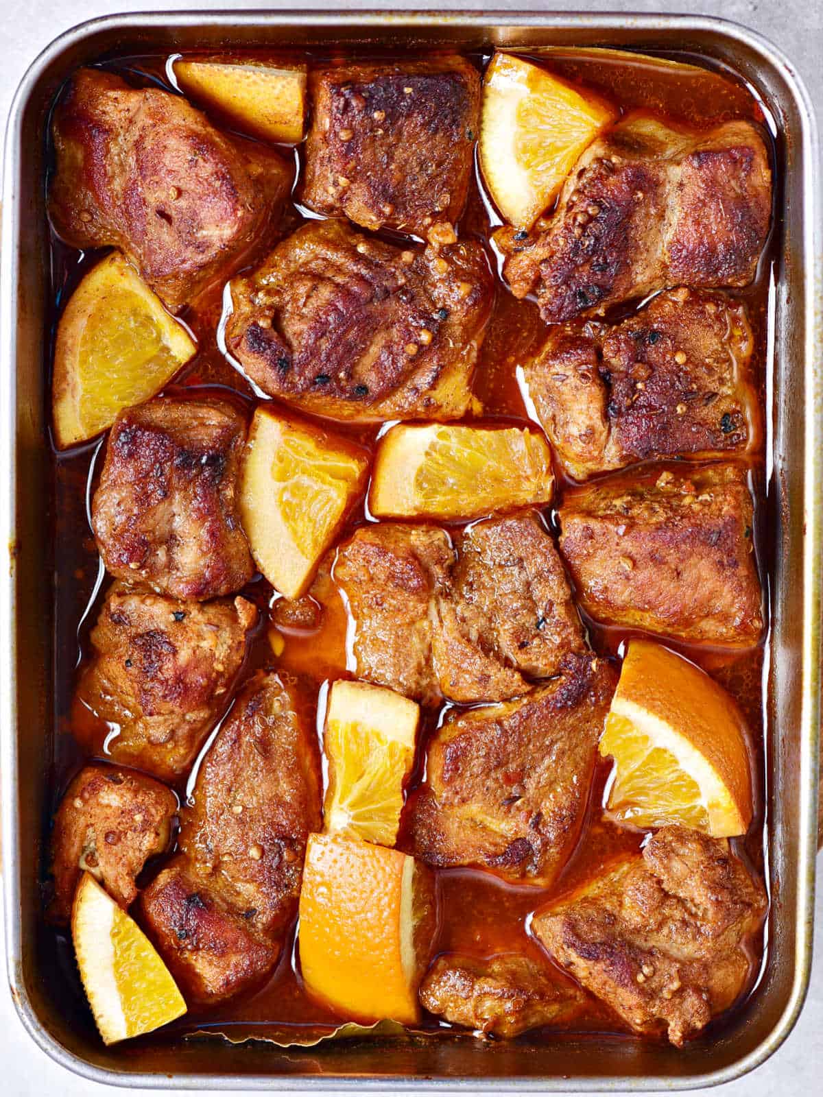 Pork shoulder pieces cooked in a baking tray with orange pieces.