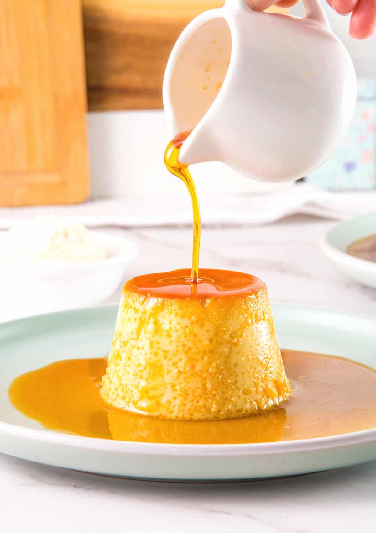 Pouring caramel on an individual flan on a plate. Wood prop on white background.