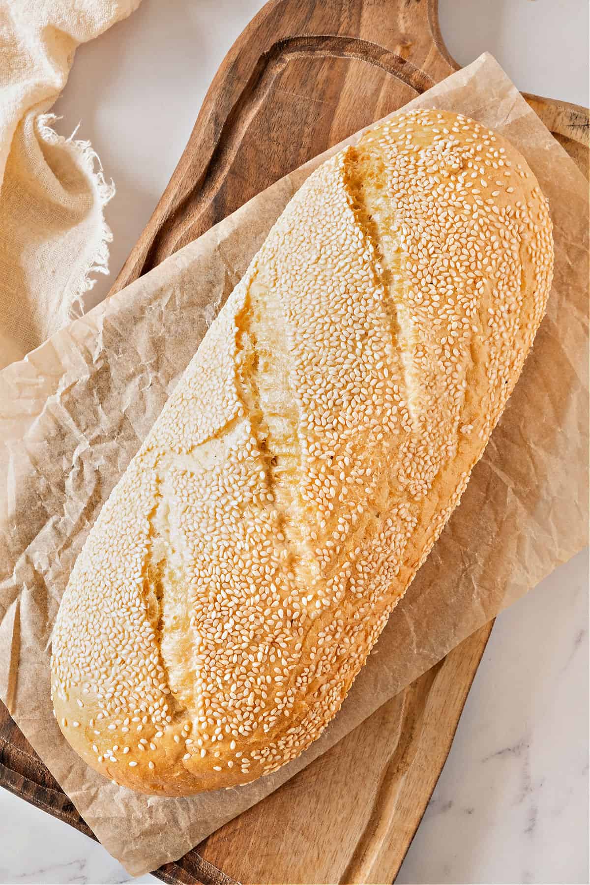 Whole loaf of sesame-coated semolina bread. Wooden board, beige cloth.