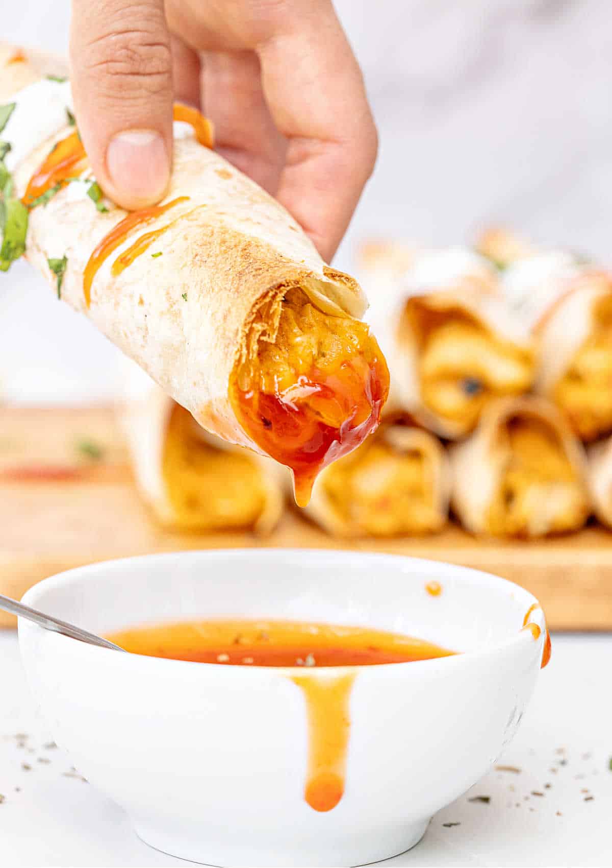 Dipped baked taquito in a white bowl with sauce. Taquitos in the marbled background.