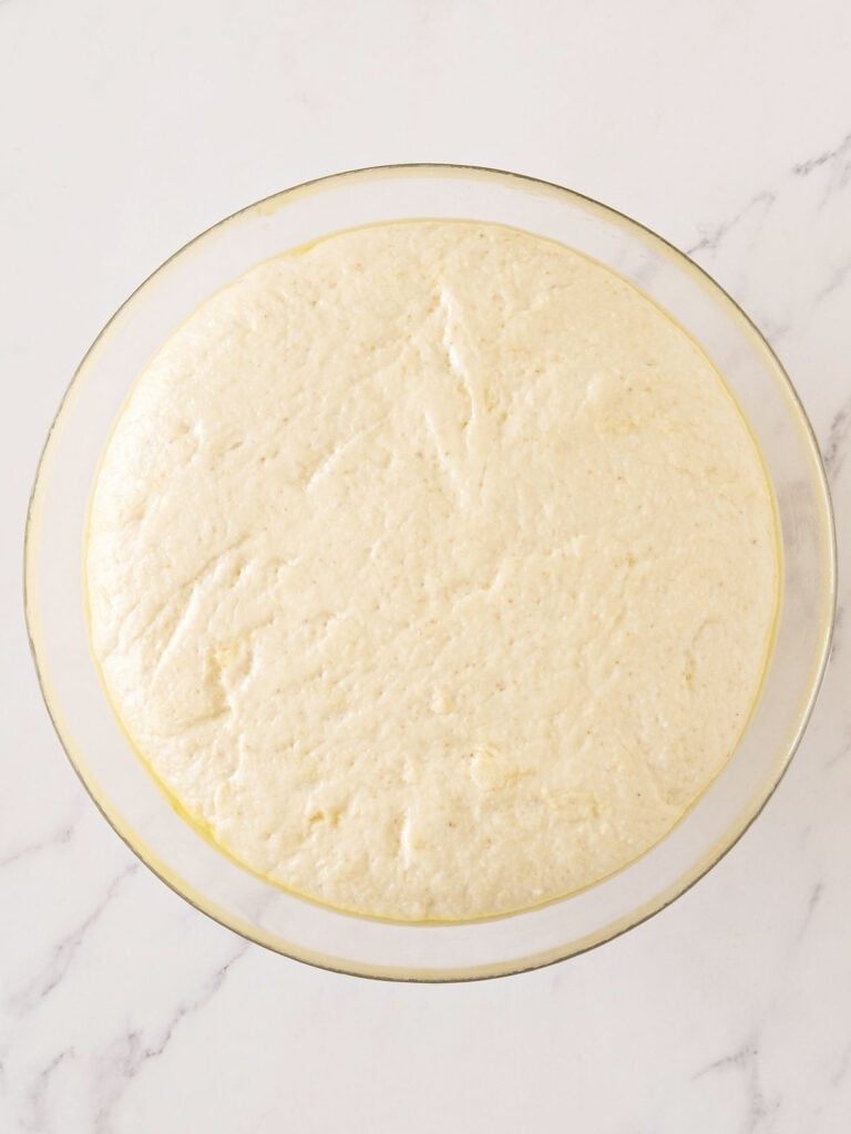 Risen bread dough in a glass bowl. White marbled background.