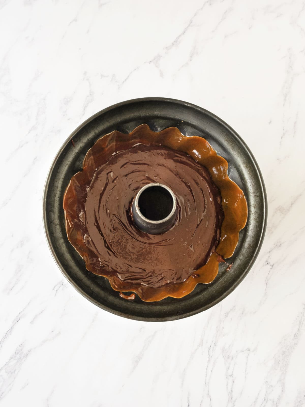 Bundt pan with caramel and chocolate layer for chocoflan. White surface. 