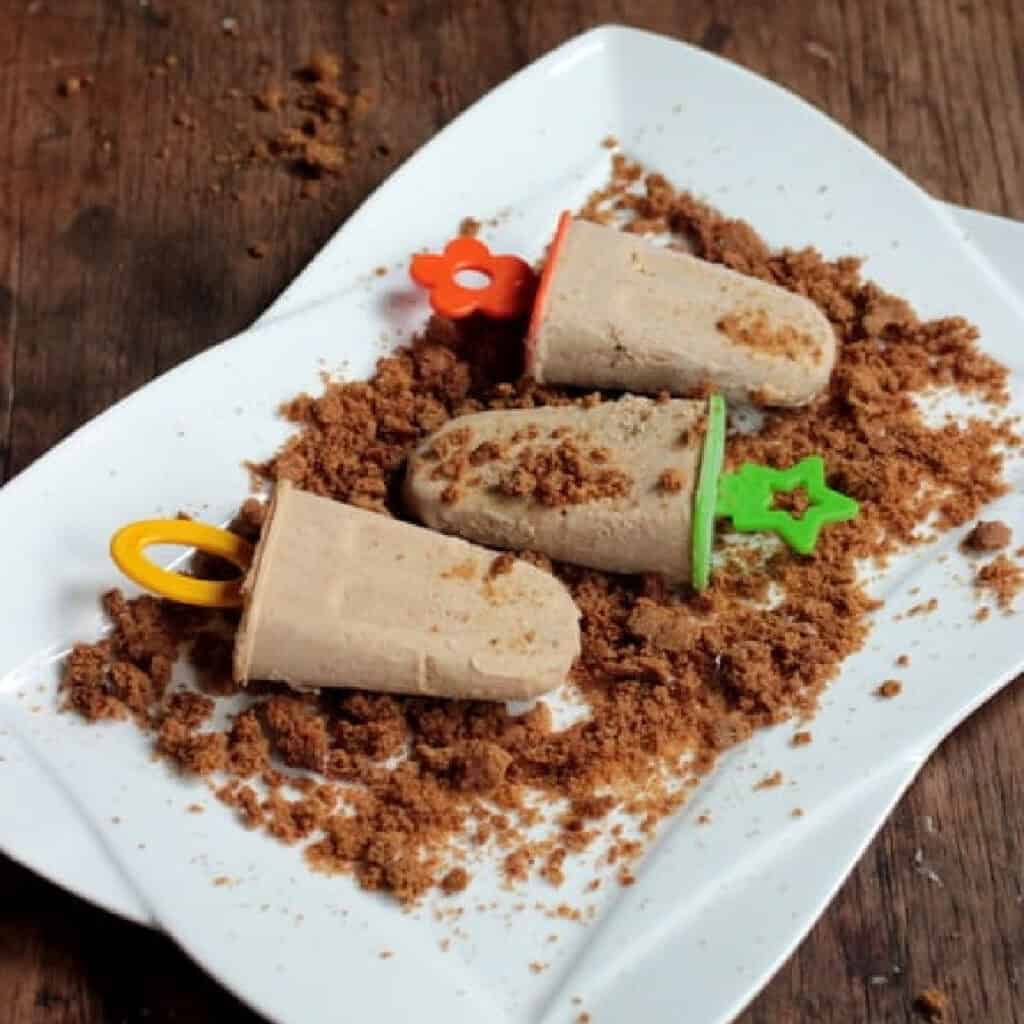 White plate with graham crumbs and cinnamon popsicles. Wooden surface.