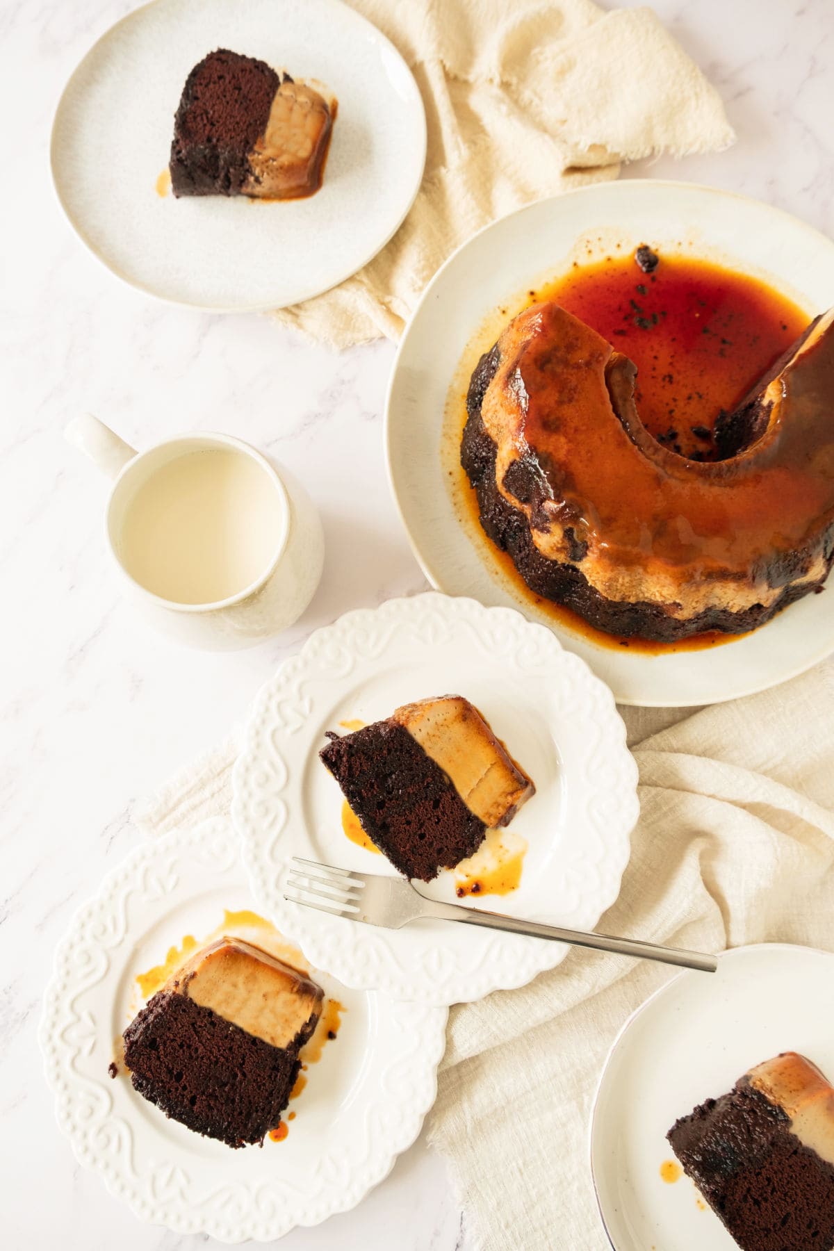 Several servings of chocoflan on white plates. Whole cake on platter. White surface.
