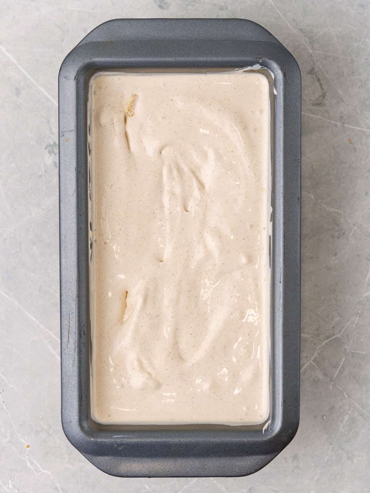 Rectangular metal loaf pan with cinnamon ice cream before freezing. Light gray surface.