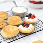 Assembling berry shortcakes on a black wire rack. Bowl of cream. White background.