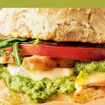 Green and white text overlay on chicken, pesto, tomato sandwich.