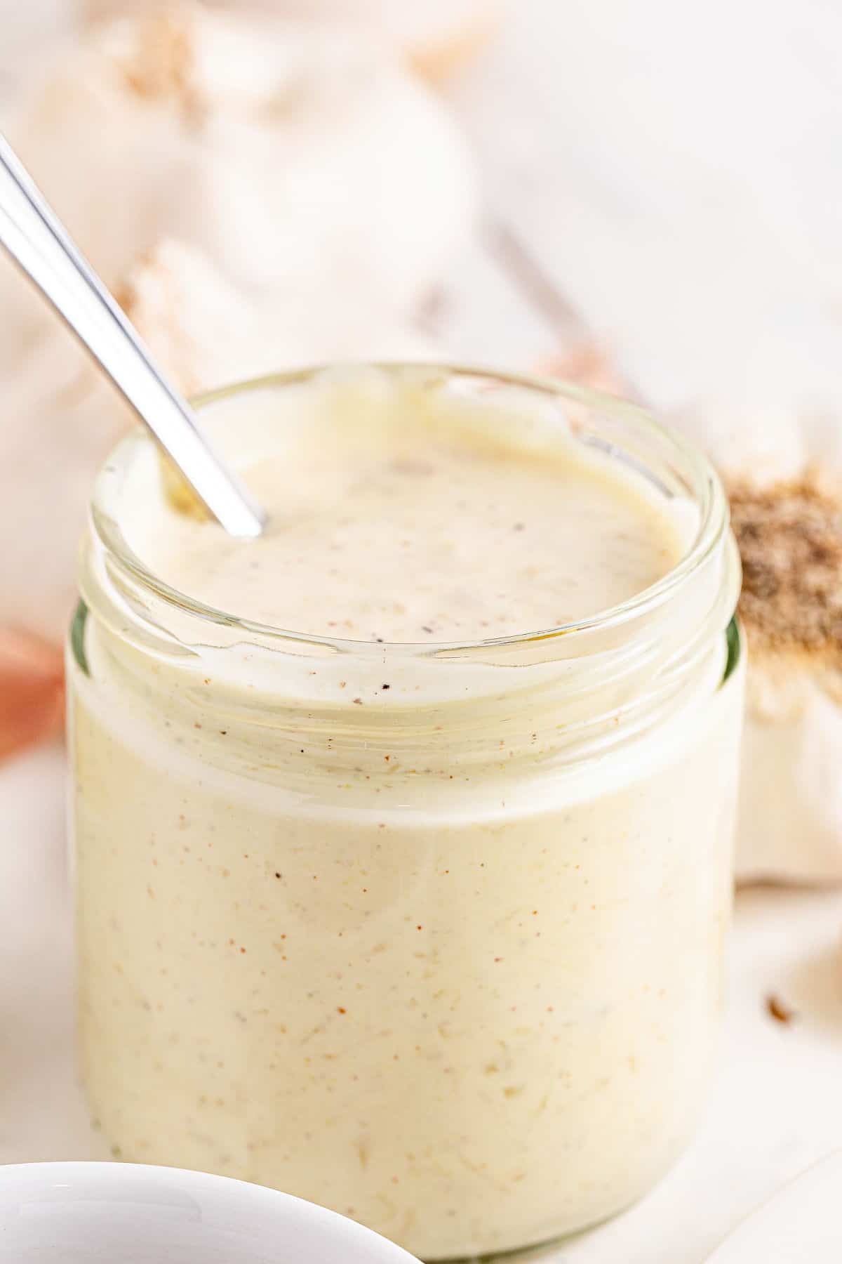 Glass container with aioli. White background with cloves.