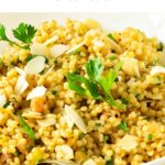 Green and white text overly on couscous salad in a white plate.