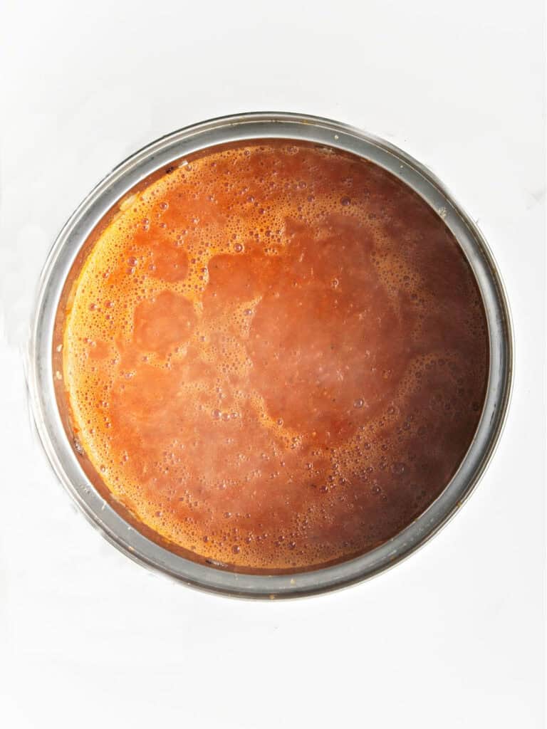 Simmering ketchup ingredients in a saucepan. White surface.