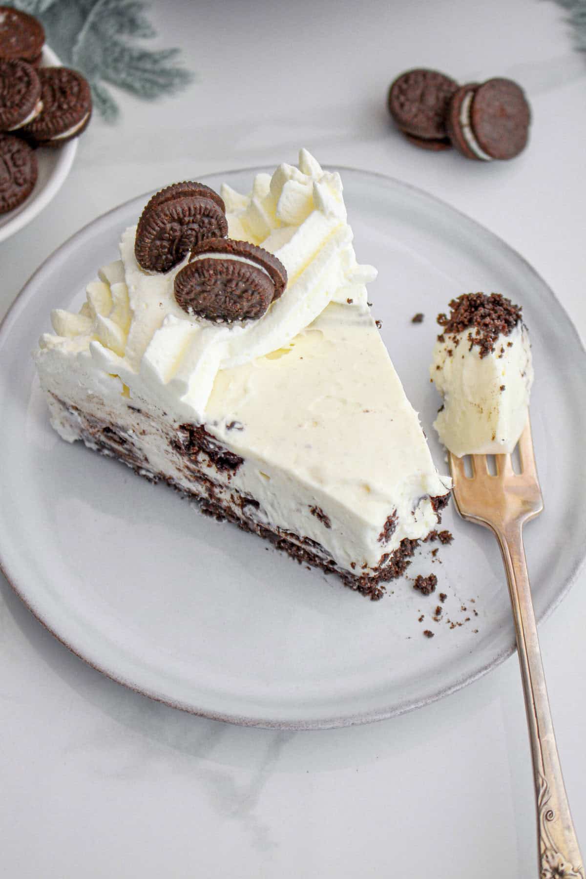 Gray plate with slice of no bake Oreo cheesecake. Silver fork with a bite.