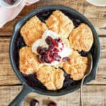 Cream topped cherry cobbler in a cast iron skillet. Wooden surface.