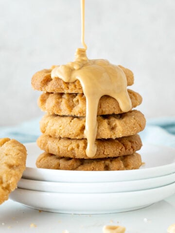 Close up of white plate with stack of cookies with pouring peanut butter. Light gray background.