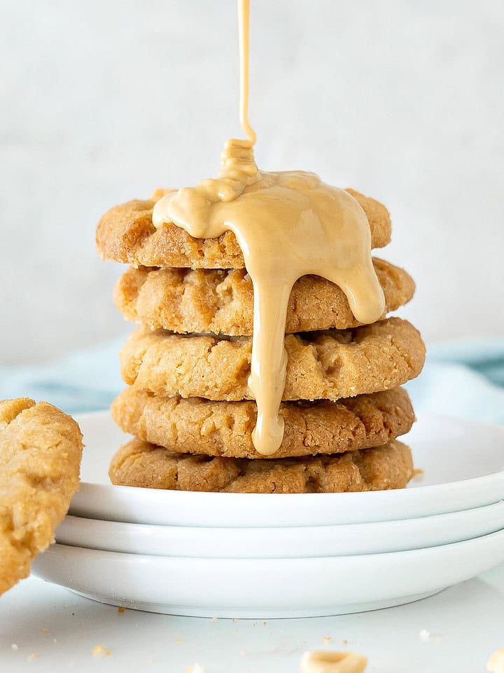 Close up of white plate with stack of cookies with pouring peanut butter. Light gray background.