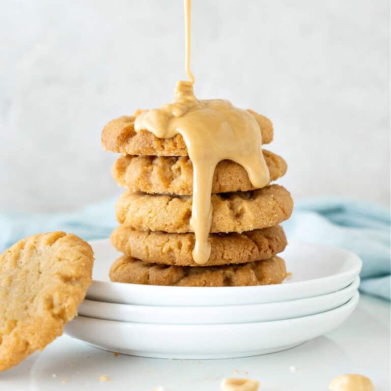 Close up of white plate with stack of cookies with pouring peanut butter. Light gray background.