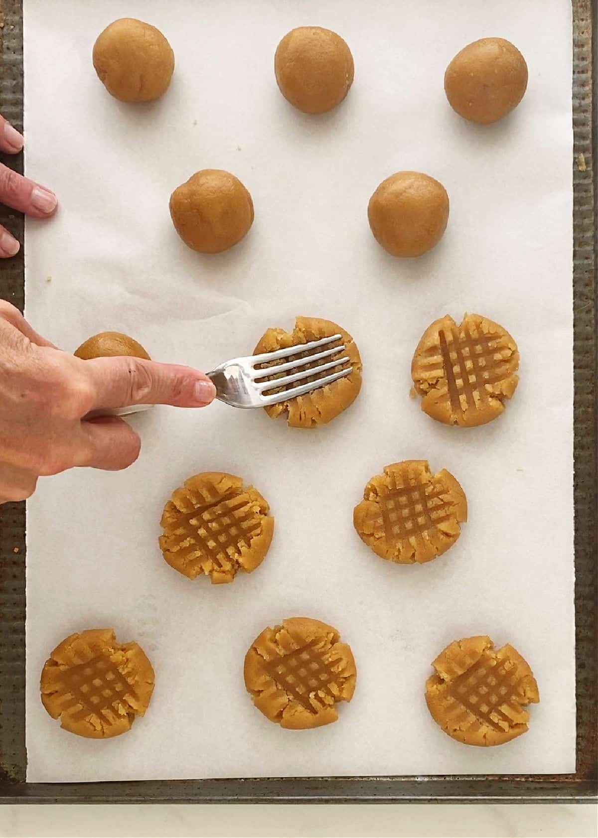 Making criss cross pattern with a fork on peanut butter cookie mounds. White paper surface.