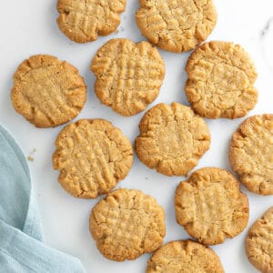 Flat peanut butter cookies on a white marbled surface. Light blue cloth.