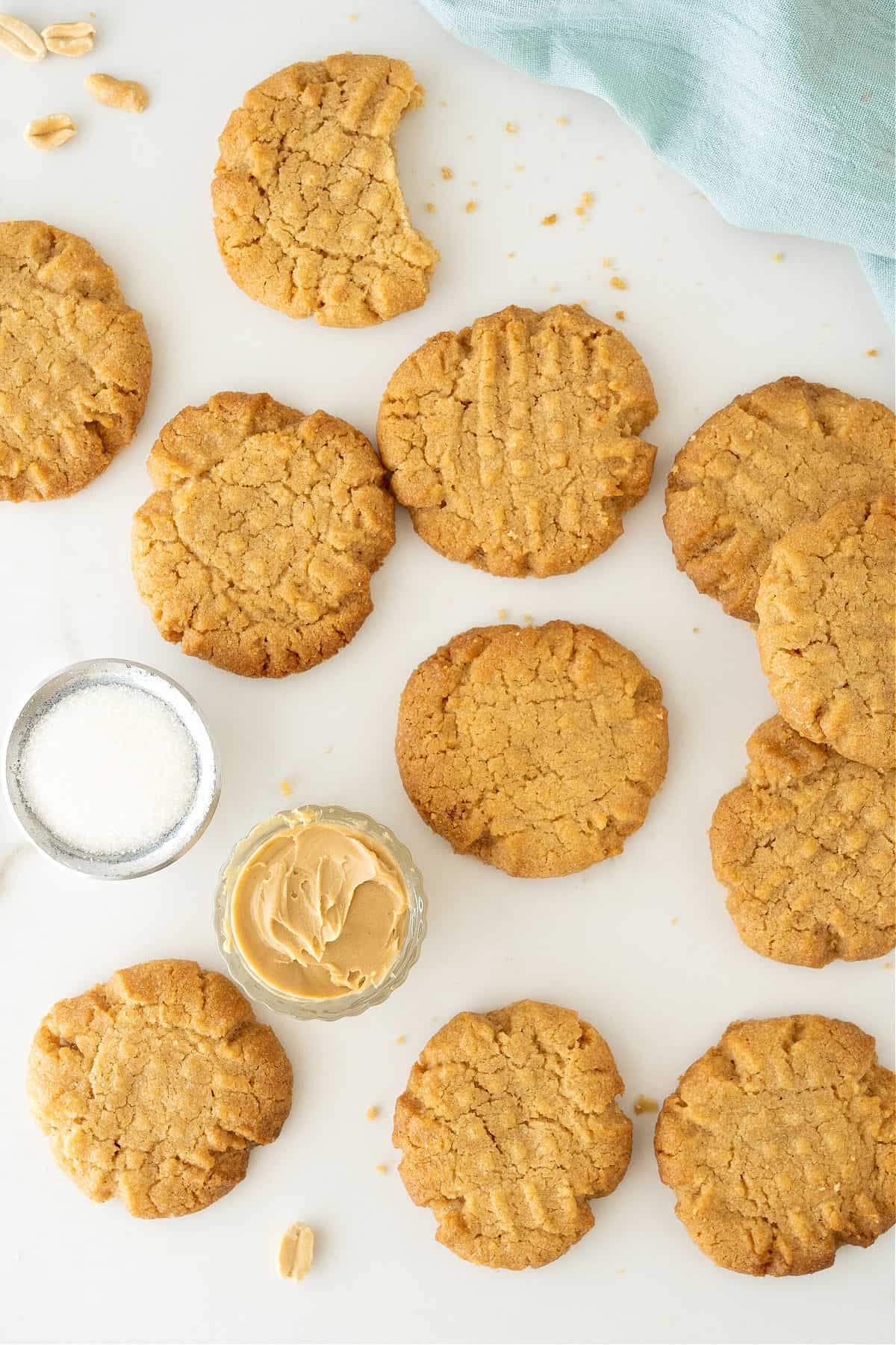 Marbled surface with several peanut butter cookies. Small bowls, blue cloth. 