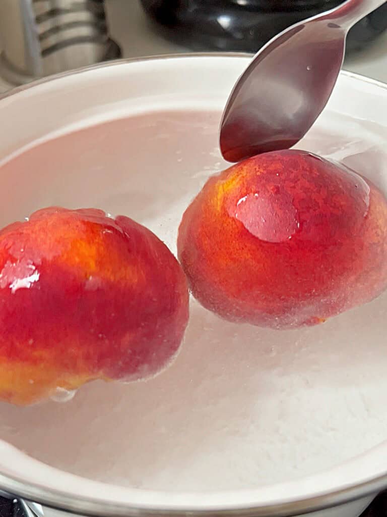 Simmering fresh peaches in a white saucepan.