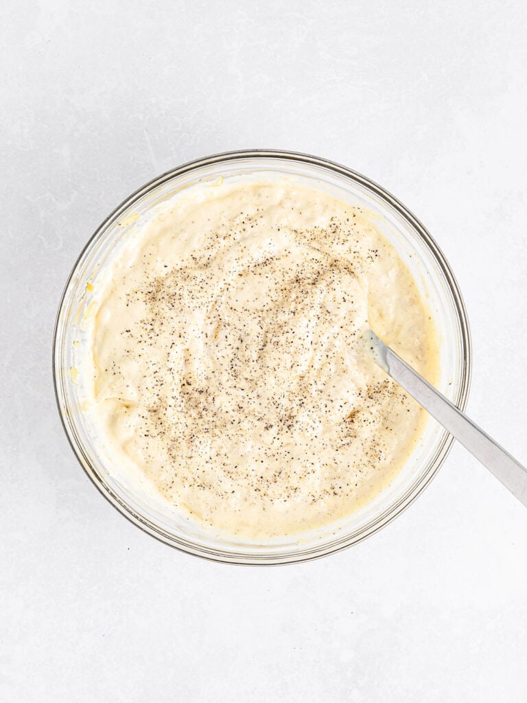 Glass bowl with aioli and a silver spoon. White surface. Top view. 