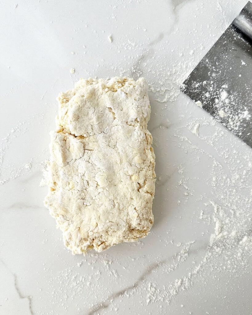 Folded shabby biscuit dough on white marble. Metal scraper.