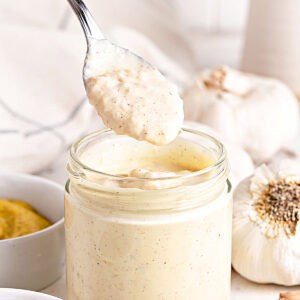 Spooning garlic aioli from a jar. Garlic heads on white background.