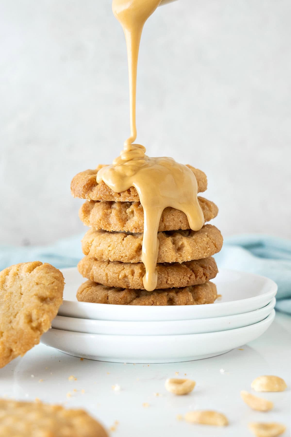 Stack of cookies on white plates with peanut butter pouring over it. Gray background.