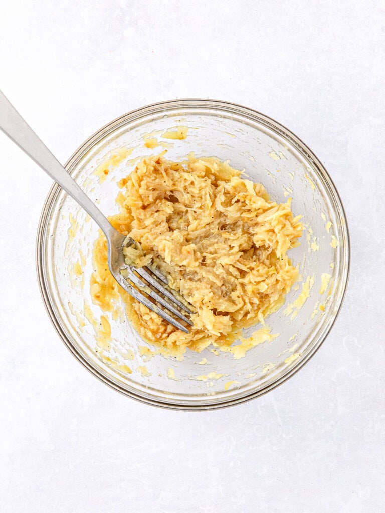 Glass bowl with mashed roasted garlic. A silver fork. White background.