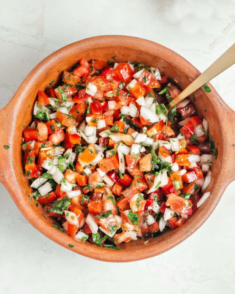 Terracotta bowl with onion, tomato, red pepper and parsley salsa. Top view.