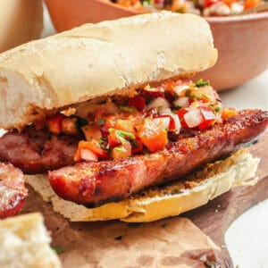 Close up chorizo chimichurri sandwich with salsa and crusty white bread, wooden board.