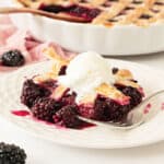 Serving of blackberry cobbler with lattice top and ice cream on a white plate. Silver fork.