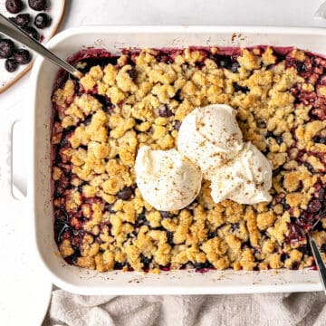 Partial top view of white dish with blueberry crumble topped with ice cream.
