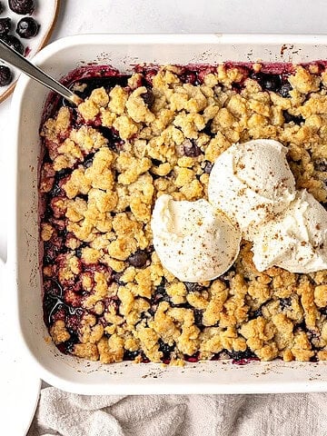 Partial top view of white dish with blueberry crumble topped with ice cream.