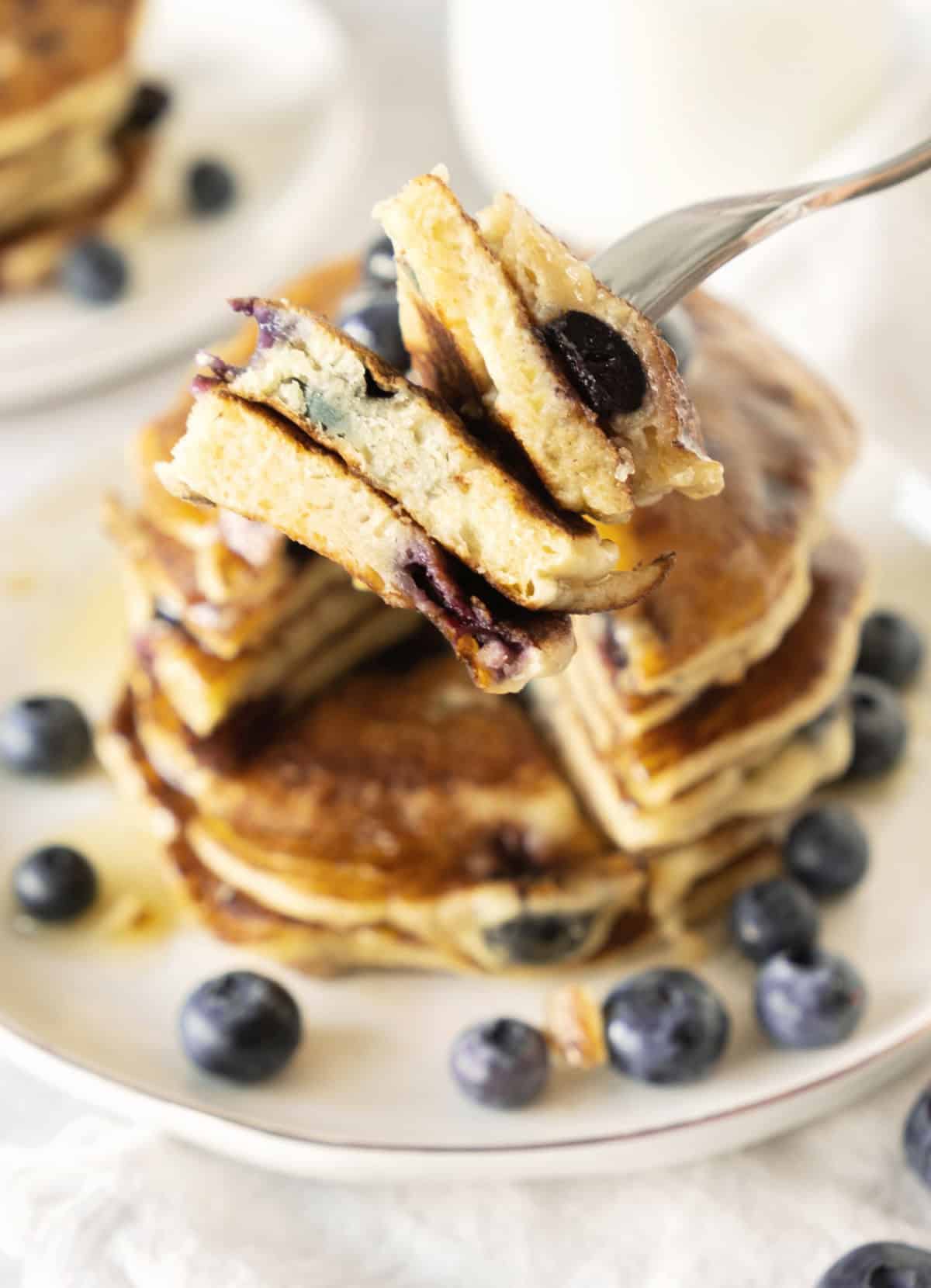 Forked pieces of blueberry ricotta pancakes. White plate with stack in the white background.