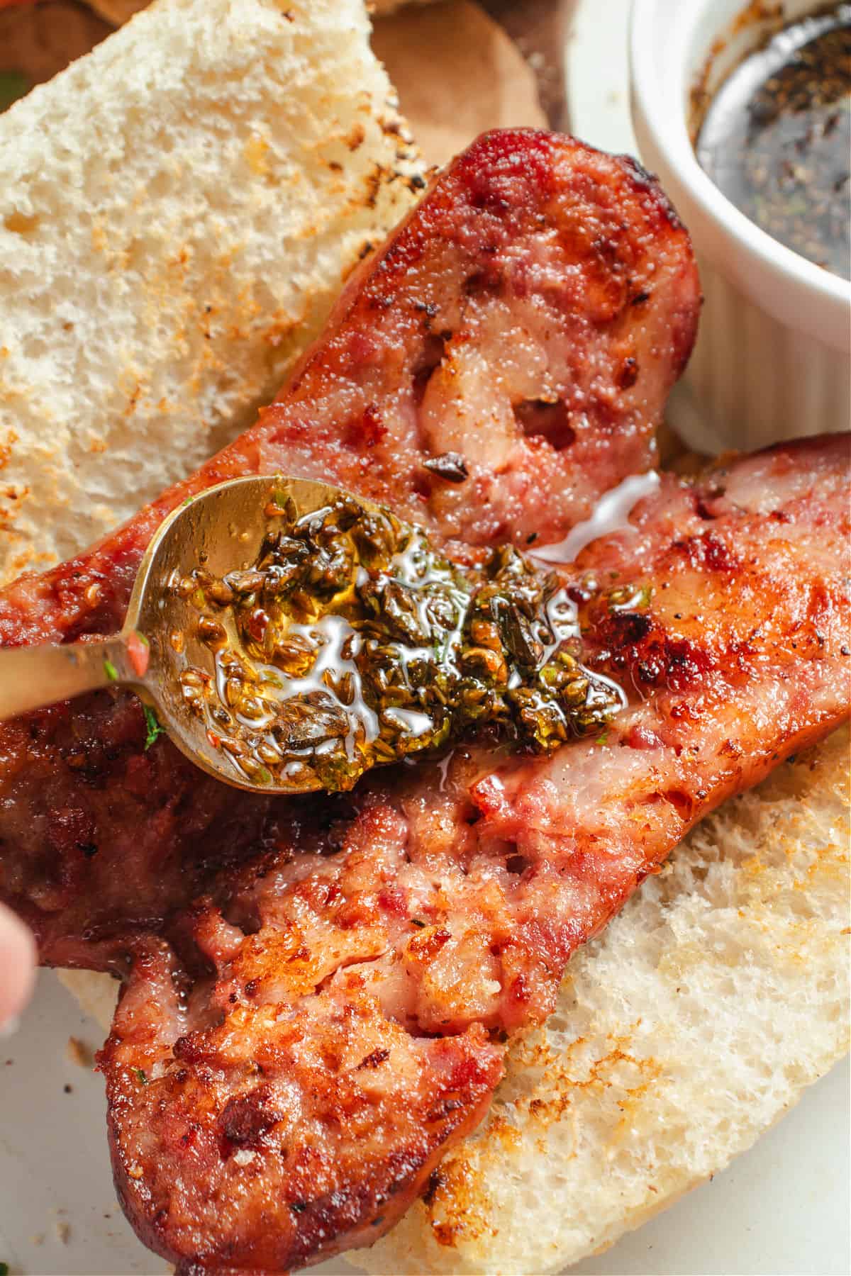 Spooning chimichurri on a chorizo sandwich.