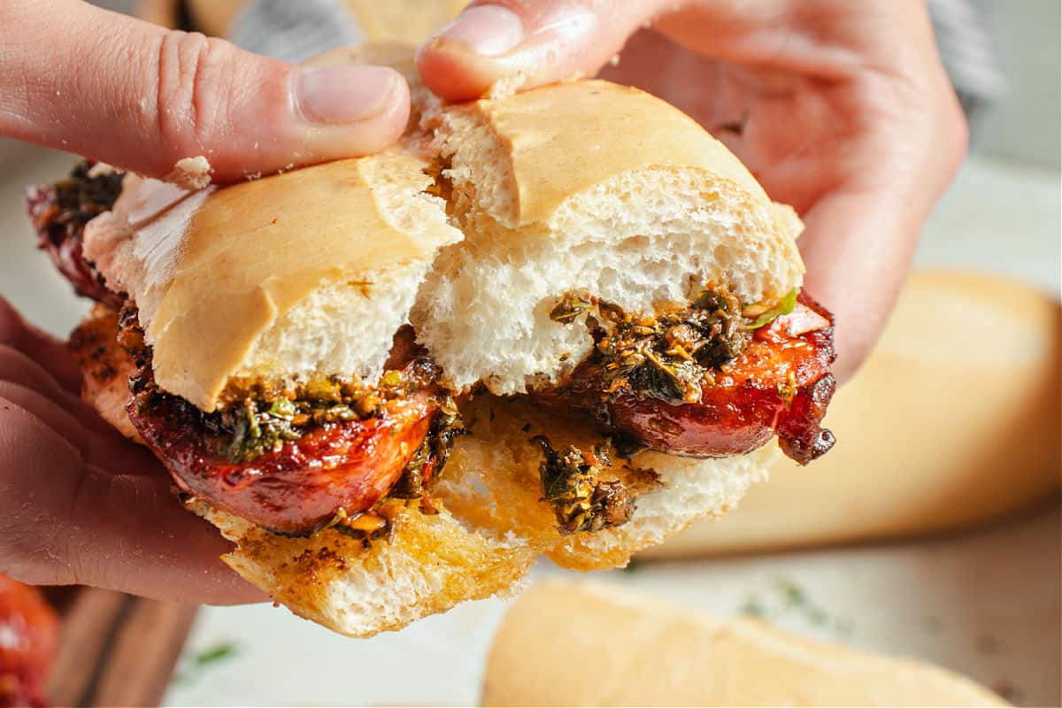 Chorizo, Chimichurri and Salsa Sandwiches Hand holding chorizo chimichurri sandwich with crusty bread.