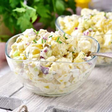 Two glass bowls with potato salad on a gray wooden board. Parsley in the background.